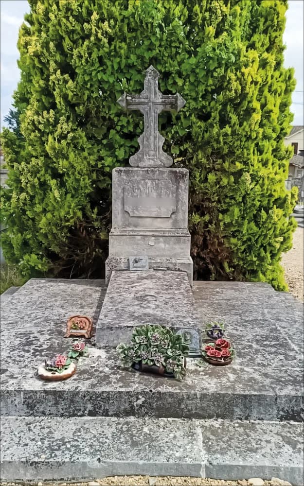 Monument surmonté d’une croix, pierre verdie par les mousses devant une haie de cyprès